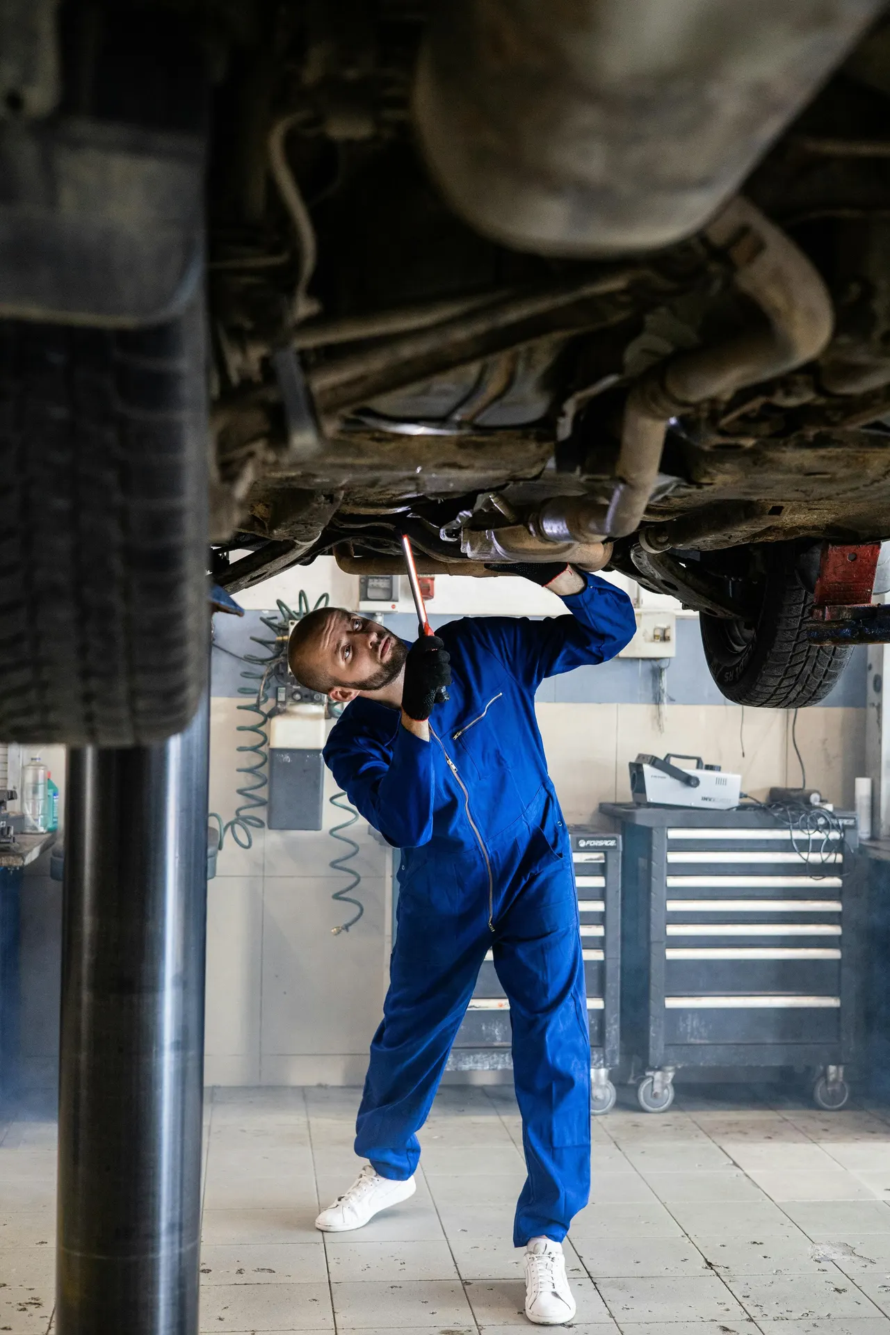 Tecnico al lavoro sotto un'auto sollevata su un ponte sollevatore d'officina